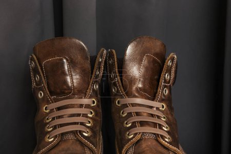 A pair of brown leather hiking boots with triple stitching and plastic laces and a gray background