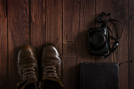 une composition avec des bottes en cuir, un vieux livre et un boîtier de caméra obscura sur une surface en bois sombre