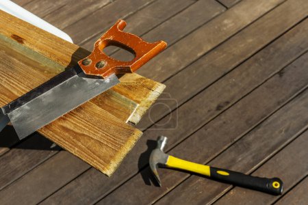 A manual carpentry saw on some wooden boards next to a hammer