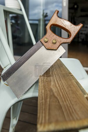 manual woodworking saw cutting a thin plank of wood on top of a blue metal chair