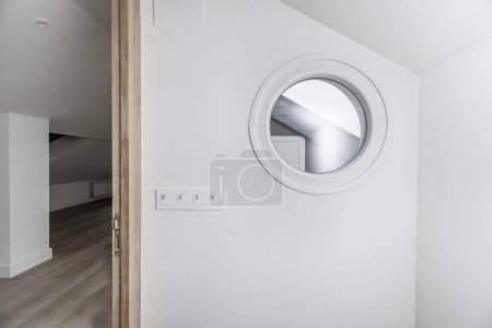 Foto de Ventana circular o portillo con marco blanco y paredes blancas, llaves de luz y acceso a otra habitación - Imagen libre de derechos