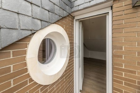 Foto de Ventana circular o portillo de una pequeña terraza con marco blanco y paredes de ladrillo marrón y puerta de aluminio blanco - Imagen libre de derechos