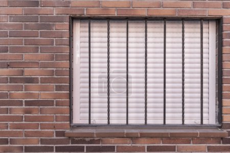 Foto de Una pared de ladrillo con una ventana con las persianas hacia abajo y una puerta de seguridad de metal - Imagen libre de derechos