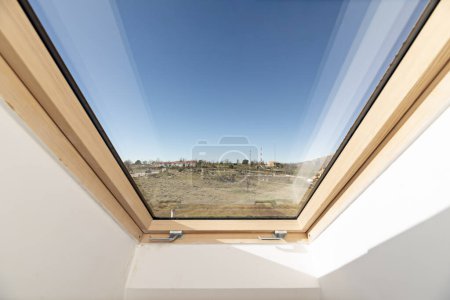 Foto de Tragaluz con estructura de madera y malla metálica de una habitación ático con vistas al campo en un día con cielos azules claros - Imagen libre de derechos