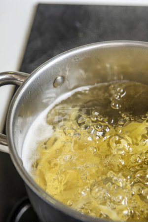 Téléchargez les photos : Une casserole d'eau bouillante pour cuire les pâtes sur une plaque vitrocéramique noire - en image libre de droit