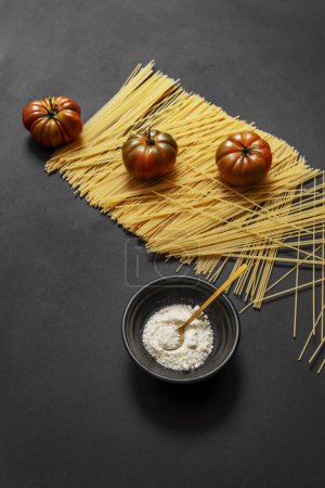 Téléchargez les photos : Quelques tomates raf brillantes sur une belle pile de spaghettis de blé et fromage râpé sur une surface noire lisse - en image libre de droit