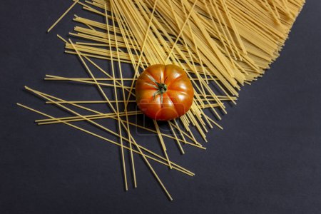 Téléchargez les photos : Tomate raf brillante sur spaghettis de blé cru et une surface noire lisse - en image libre de droit