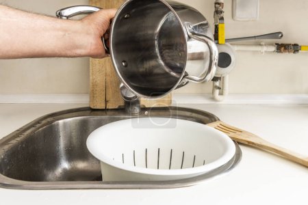 Emptying water from a pot onto a drainer in a kitchen sink
