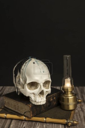 un crâne blanc avec des dents supérieures sur un vieux livre à côté d'une petite lampe Argand