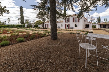Mesa de metal blanco con sillas a la sombra entre jardines con suelos de terracota y grava en el patio de una casa rural andaluza