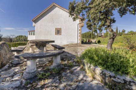 Téléchargez les photos : Une maison de campagne avec des façades blanches, des sols en pierre sur le terrain et une table avec des bancs de ciment - en image libre de droit
