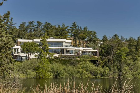 Téléchargez les photos : Une belle maison de maître de style moderne entourée d'arbres sur la rive d'un lac - en image libre de droit