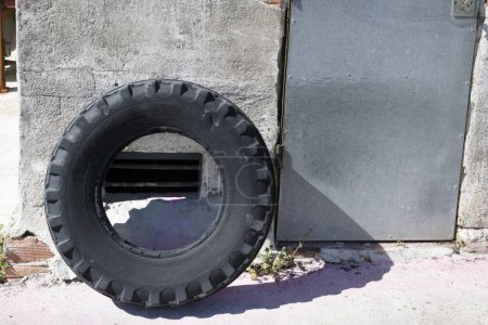 An old rubber wheel leaning on a wall with a metal door