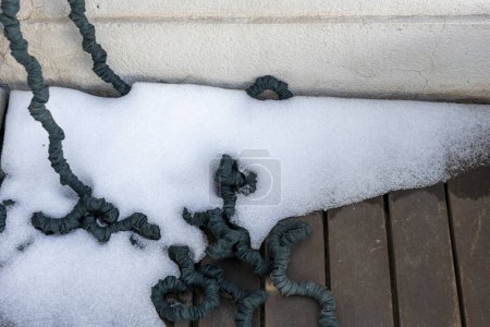 Ecke einer Terrasse mit angesammeltem Eis und einem elastischen Schlauch zwischen dem Eis