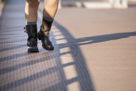 Patas de mujer con botas de siete leguas dando un paseo sobre una superficie metálica