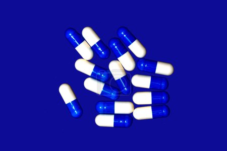 blaue und weiße Medikamentenkapseln auf blauem Hintergrund abstraktes Konzept.