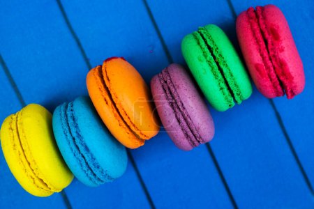 Topshot of sweet and colourful french macaroons on blue wooden background.