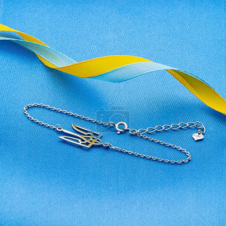 Photo for Jewelery patriotic decoration - an accessory made of rhodium-plated silver. Anchor chain bracelet with Ukrainian coat of arms trident on denim bluebackground and a spiral ribbon with an abstract serpentine of yellow-blue colors. Glory to Ukraine. - Royalty Free Image
