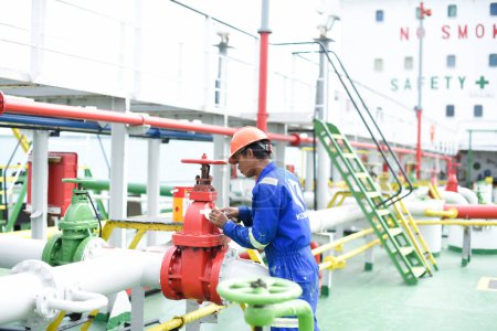 Foto de Banten, Indonesia, 15 de noviembre de 2022: Miembros de la tripulación revisando válvulas de tuberías químicas al aire libre a bordo del buque. Concepto de mantenimiento de buques. Concepto de trabajo en equipo. - Imagen libre de derechos