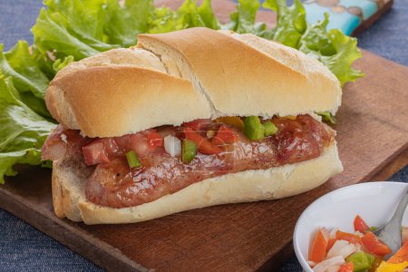 Choripan, typical argentine sandwich with chorizo and creole sauce on a wooden board.