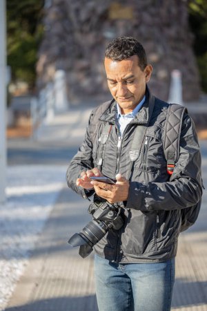 Téléchargez les photos : Photographe travaillant dans la rue et envoyant des SMS avec son téléphone portable. - en image libre de droit