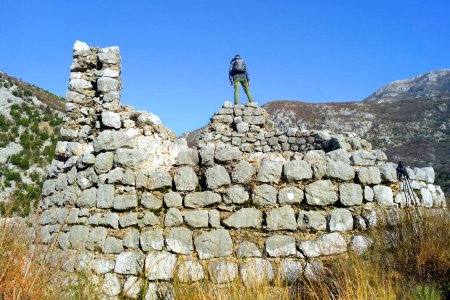 Un turista con una mochila de pie sobre las ruinas de una gran torre redonda en la colina Gradina (Risan, Montenegro)
