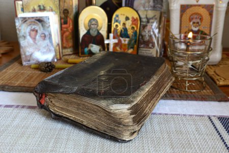 Old antique and damaged sacred religious book of Holy Bible in leather binding In front of home small iconostasis. Selective focus. The concept of Orthodoxy.