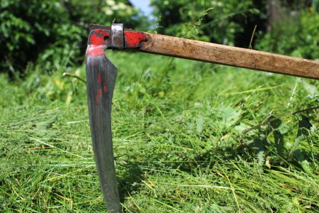 Hand scythe on the background of green grass. The tradition of mowing grass on a green meadow. Agricultural machinery. Preparation of fodder for livestock.