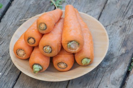 Photo for Bunch of fresh carrots on a wooden plate on a wooden table. - Royalty Free Image