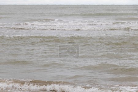 Photo of the sea with small waves, seen from an angle at eye level. The water is gray and slightly brown in color.