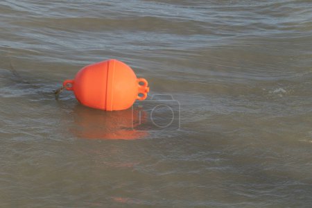 Une photo d'une bouée en plastique orange flottant dans la mer.