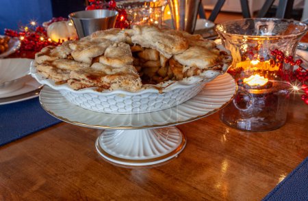 Homemade gourmet apple pie on a holiday table with candles and lights.