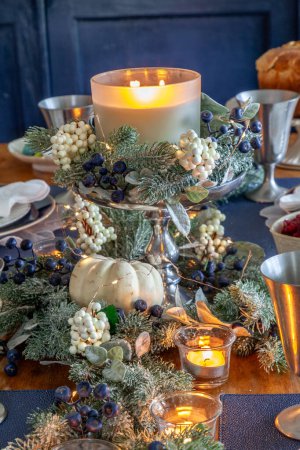 Festive candles and greenery on a table with fine bone China and a silver serving spoon at Christmas.