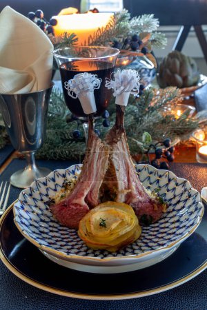 Lammkotelett auf einem Festtagstisch mit gedämpfter Artischocke, Kartoffeln und auf einem Knochenteller mit Kerzen und Feiertagsdekor.