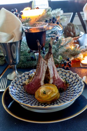 Lammkotelett auf einem Festtagstisch mit gedämpfter Artischocke, Kartoffeln und auf einem Knochenteller mit Kerzen und Feiertagsdekor.
