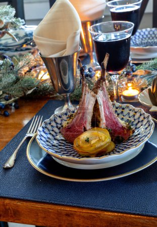Lamb chop on a holiday table with steamed artichoke, potatoes and on a bone China plate with candles and holiday decor.