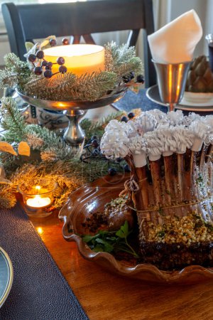Bastidor de cordero en una mesa de vacaciones con alcachofa al vapor, patatas y en un hueso plato de China con velas y decoración navideña.