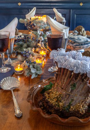 Rack of lamb on a holiday table with steamed artichoke, potatoes and on a bone China plate with candles and holiday decor.
