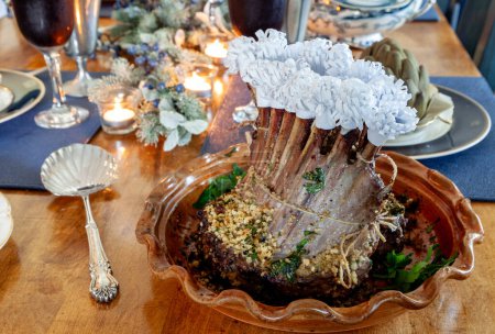 Bastidor de cordero en una mesa de vacaciones con alcachofa al vapor, patatas y en un hueso plato de China con velas y decoración navideña.