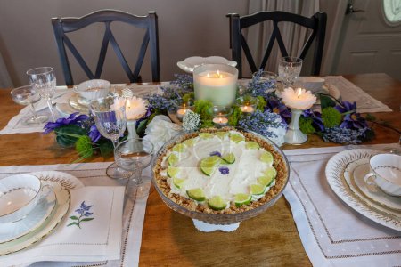 Key lime Cheesecake on an antique cake stand on a table set with candles and flowers.