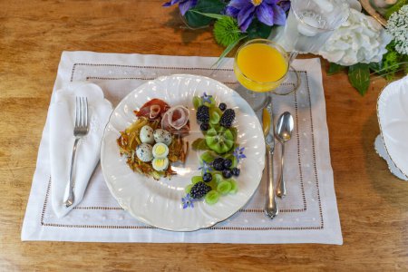Quail eggs on a hashbrown potato nest with prosciutto and decorative fruit.