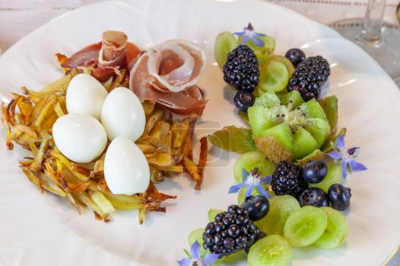 Téléchargez les photos : Œufs de caille sur un nid de pommes de terre hashbrown avec prosciutto et fruits décoratifs. - en image libre de droit