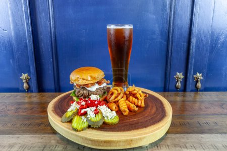 Gourmet Grilled burger with bacon and gorgonzola cheese on a brioche bun with beer and French fries.