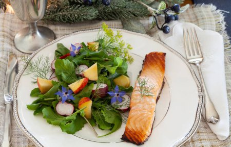 Foto de Ensalada de verduras ecológicas con flores de borraja púrpura, rúcula, rábano y salmón en un plato fino de China con cubiertos elegantes. - Imagen libre de derechos