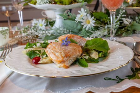Lachsherzen auf frühlingshaftem grünem Salat auf feinen China-Tellern und Kristall mit Goldeinlage auf formeller Tischdekoration.