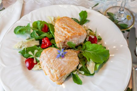 Coeurs de saumon sur une salade verte printanière servie sur de fines assiettes de Chine et du cristal avec incrustation d'or sur une table formelle.