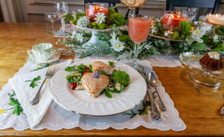 Lachsherzen auf frühlingshaftem grünem Salat auf feinen China-Tellern und Kristall mit Goldeinlage auf formeller Tischdekoration.