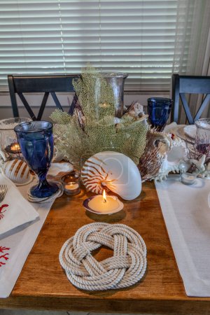 Decoración de concha y vela en una mesa náutica con colores naturales y azul profundo.