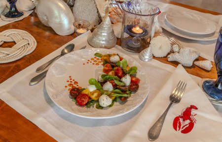 Seafood mix and Caprese salad with cherry tomatoes, mozzarella, basil, and arugula on a nice plate with a seashell decor table.