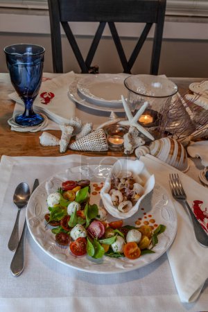 Meeresfrüchte-Mischung und Caprese-Salat mit Kirschtomaten, Mozzarella, Basilikum und Rucola auf einem schönen Teller mit Muscheldekor.